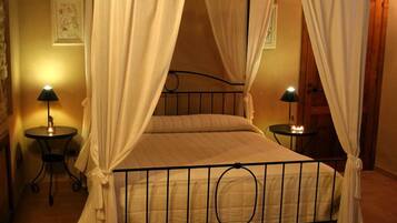 A four-poster bed with white curtains, two bedside tables with lamps, and a framed picture on the wall.