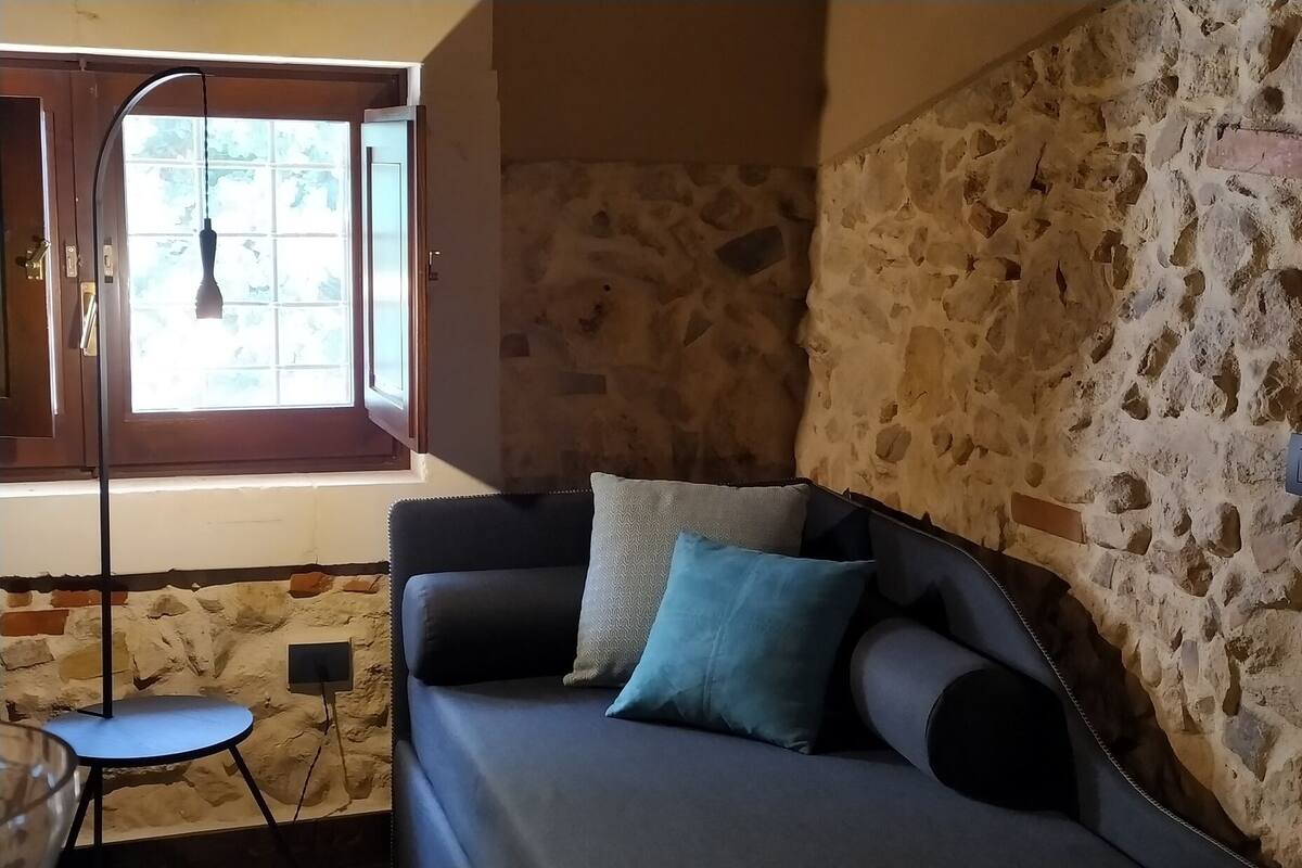 A room with a stone wall, a sofa with cushions, a small round table, and a window with a view.