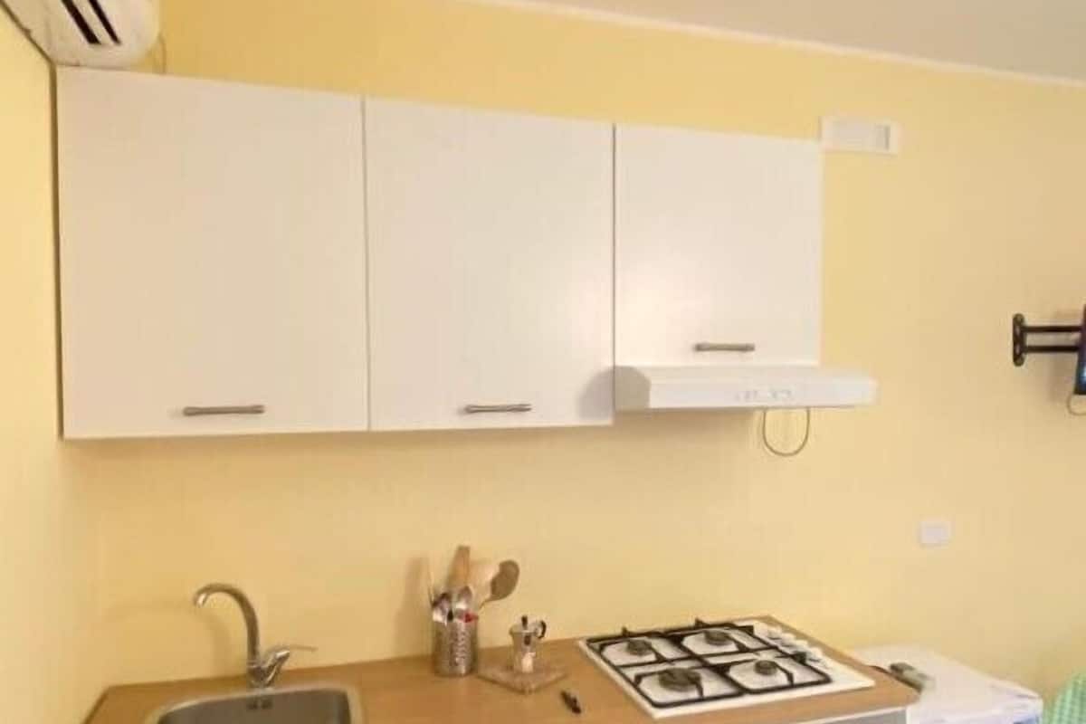 A compact kitchen with white cabinets, a sink, a gas stove, and a small refrigerator.