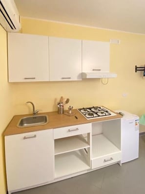 A compact kitchen with white cabinets, a sink, a gas stove, and a small refrigerator.