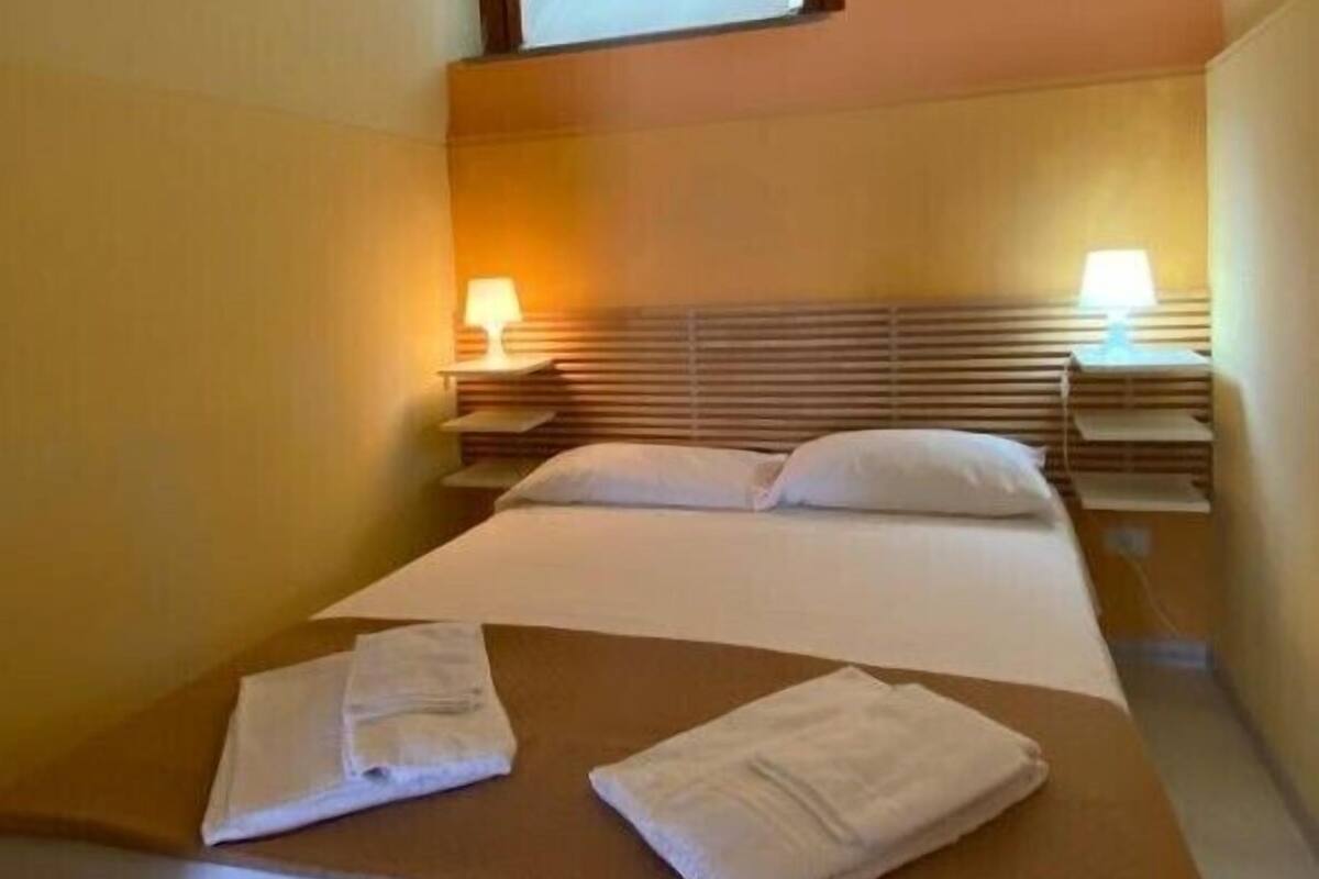 A hotel room with a bed, two bedside tables, and a window.