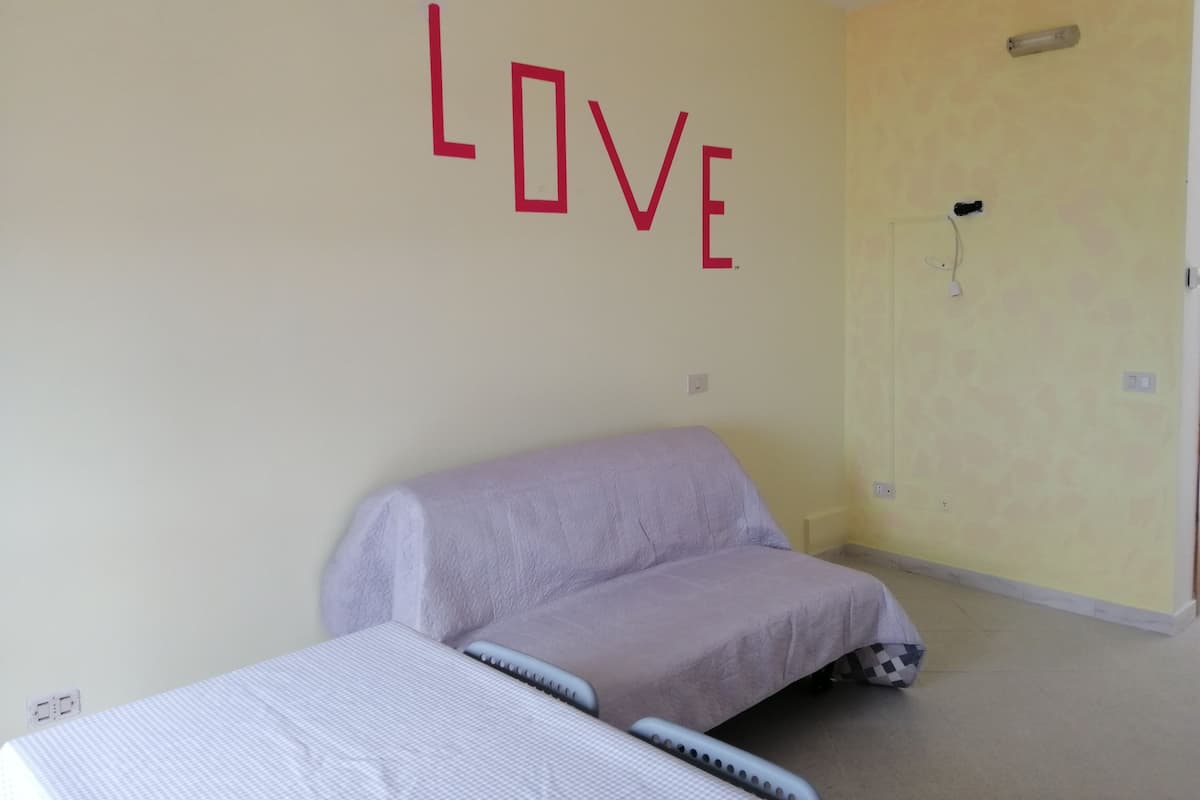 A room with a bed, a chair, a wall with the word "LOVE" in red letters, and a door with a light switch.