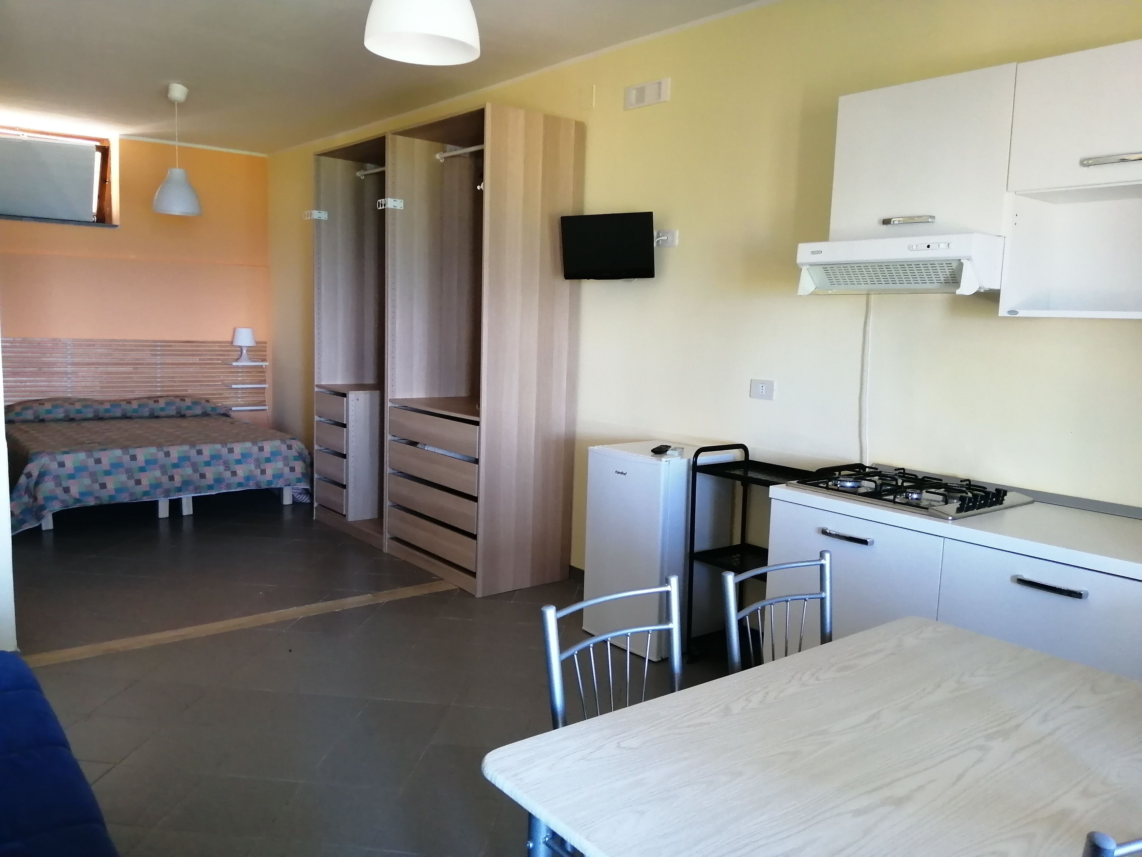 A compact room with a bed, a small kitchenette, and a dining area.