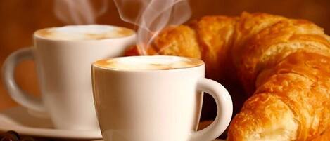 Two white cups of coffee with steam, a croissant, and coffee beans on a wooden surface.