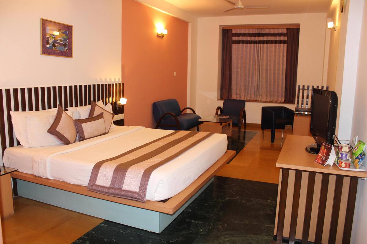 A hotel room with a bed, two chairs, a desk with a computer, and a television.