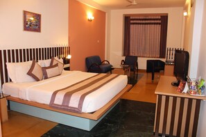 A hotel room with a bed, two chairs, a desk with a computer, and a television. - Capitol Hill (Ranchi)