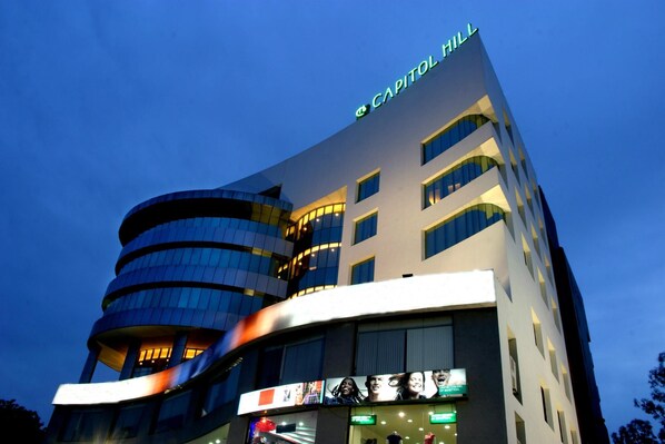 A modern hotel with a curved facade, multiple floors, and illuminated signage. - Capitol Hill (Ranchi)