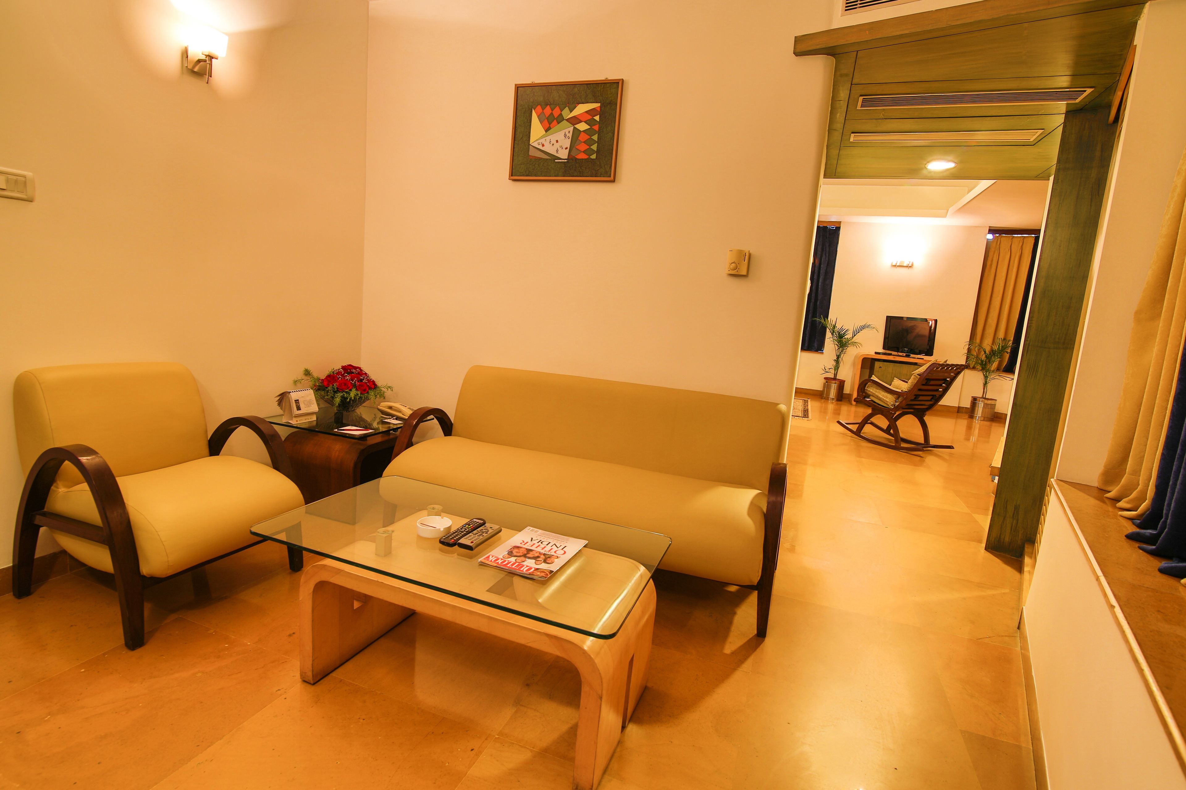 Ein Wohnzimmer mit einer Couch, zwei Sesseln, einem Glastisch, einem Fernseher und einem Gemälde an der Wand.