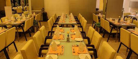 Une salle de conférence avec plusieurs tables dressées pour un repas, équipée de chaises et de couverts.