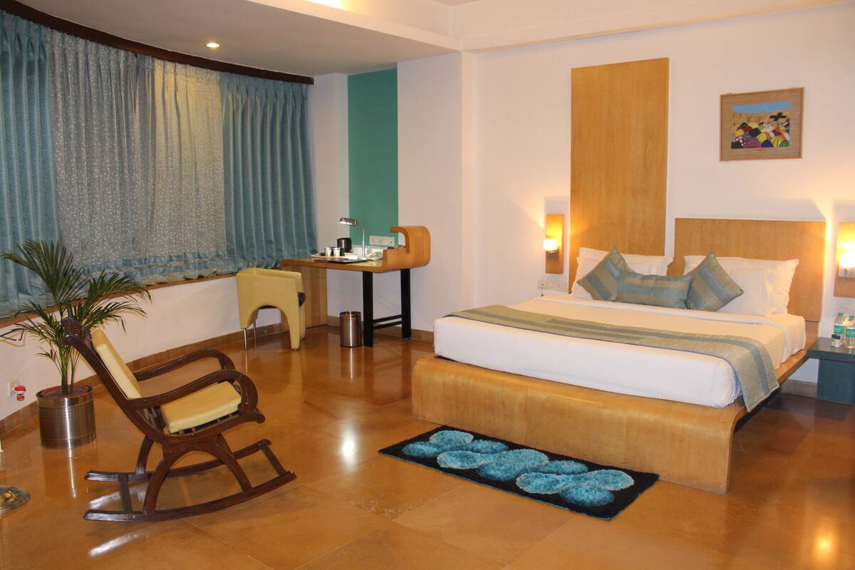 A hotel room with a large bed, a desk, a rocking chair, and a potted plant.