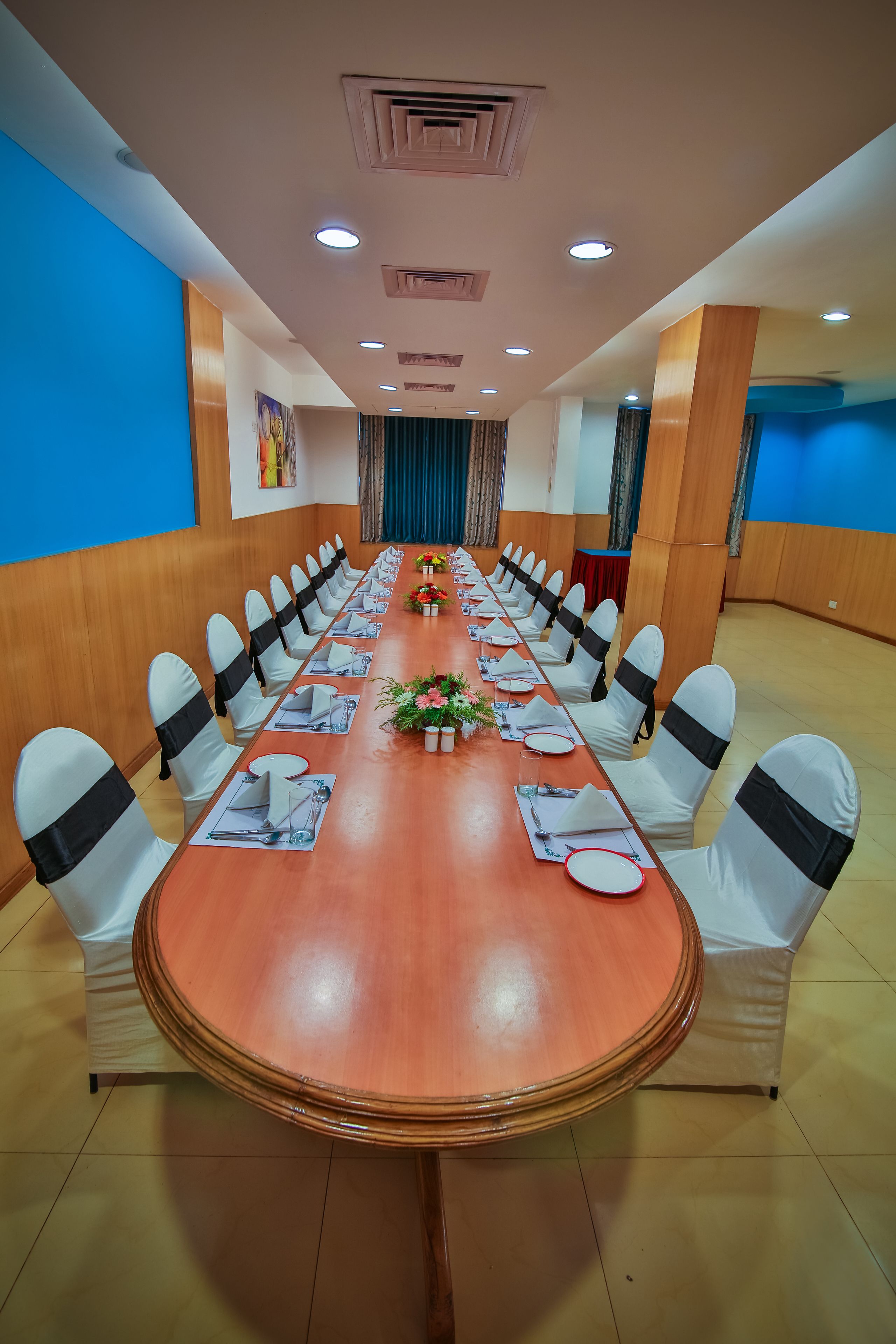 A conference room with a long table, white chairs with black sashes, and a blue accent wall.