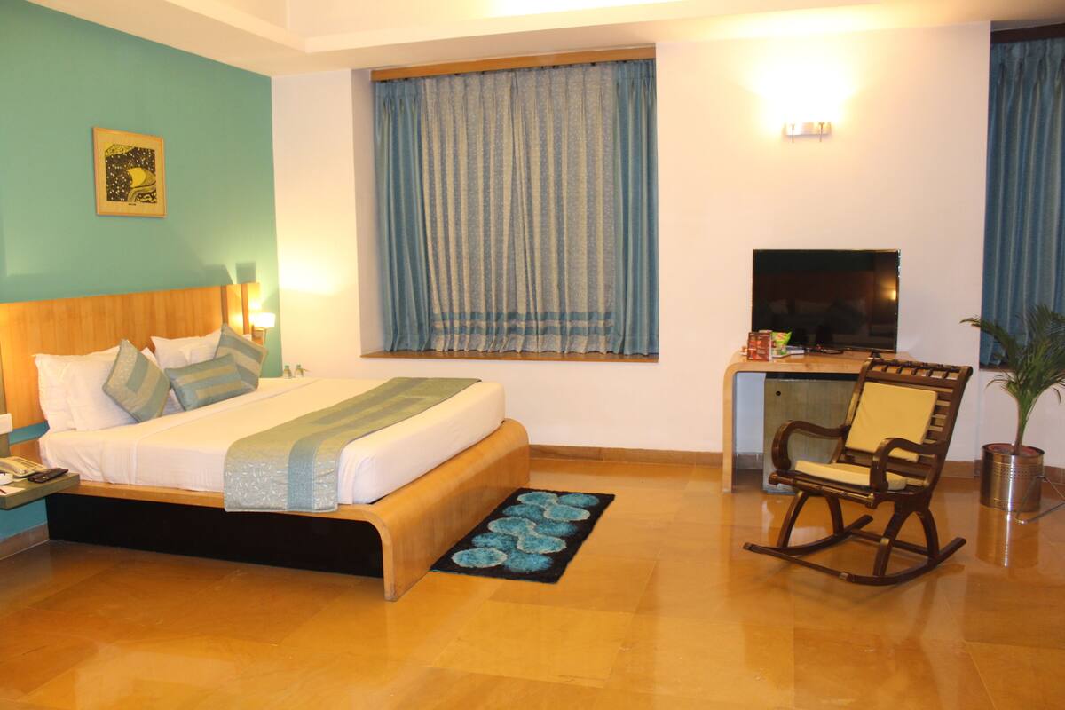A hotel room with a bed, a desk, a TV, and a rocking chair.