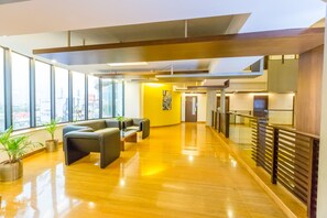 A spacious lobby with a wooden floor, seating area, and large windows offering a view of the city. - Capitol Hill (Ranchi)