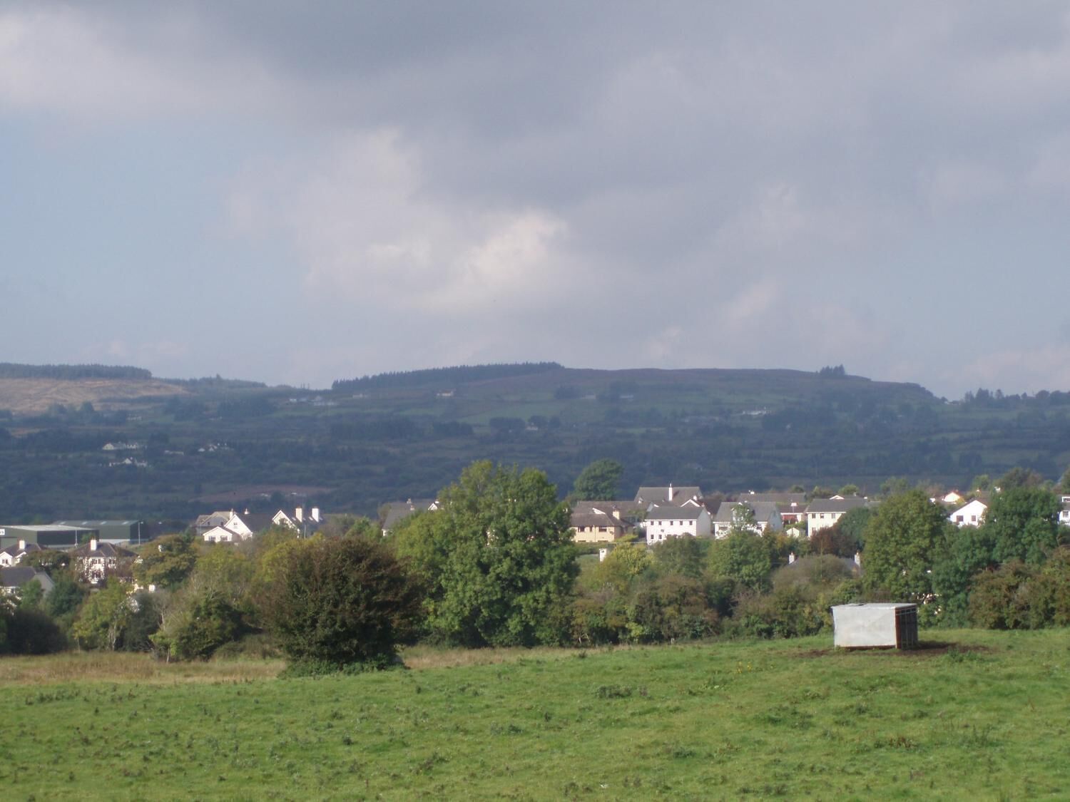 Un paysage rural avec des maisons, un petit abri et une colline en arrière-plan.