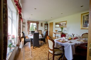 Un comedor con suelo de madera, una mesa de comedor preparada para cuatro personas y una ventana con cortinas.