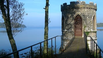 A stone tower with a wooden door, surrounded by trees and a calm lake.