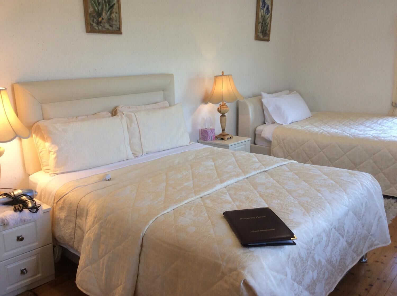 Ett hotellrum med två sängar, var och en med ett vadderat sängöverkast och kuddar. Det finns ett nattduksbord med en lampa och en bok med titeln "Reading House".