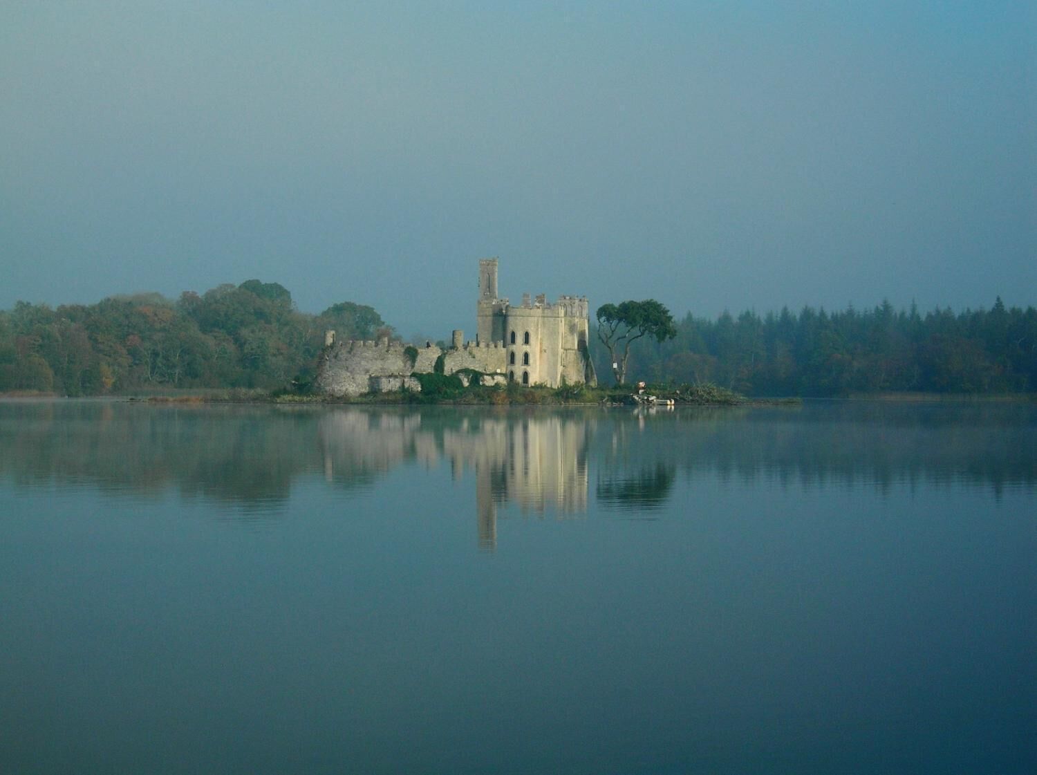 Un castillo histórico en una isla rodeada de aguas tranquilas, con un bosque en el fondo.
