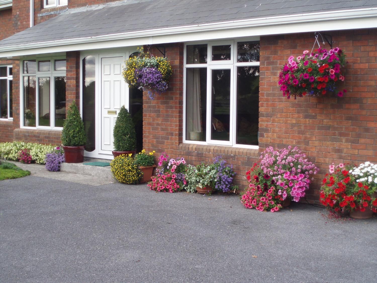 A brick building with a white front door, multiple windows, and hanging flower baskets.