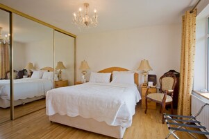 Una habitación de hotel con una cama grande, dos mesitas de noche con lámparas, una silla, un espejo y un candelabro.