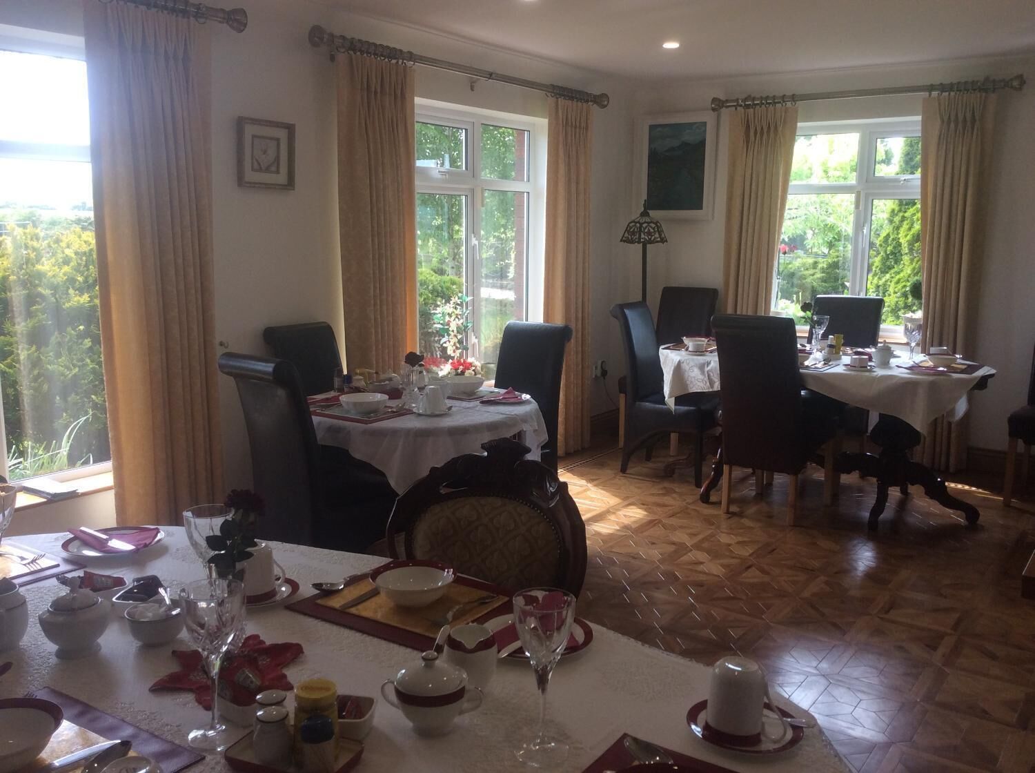 Comedor con dos mesas dispuestas para comer, ventanas amplias con cortinas y vistas al exterior.