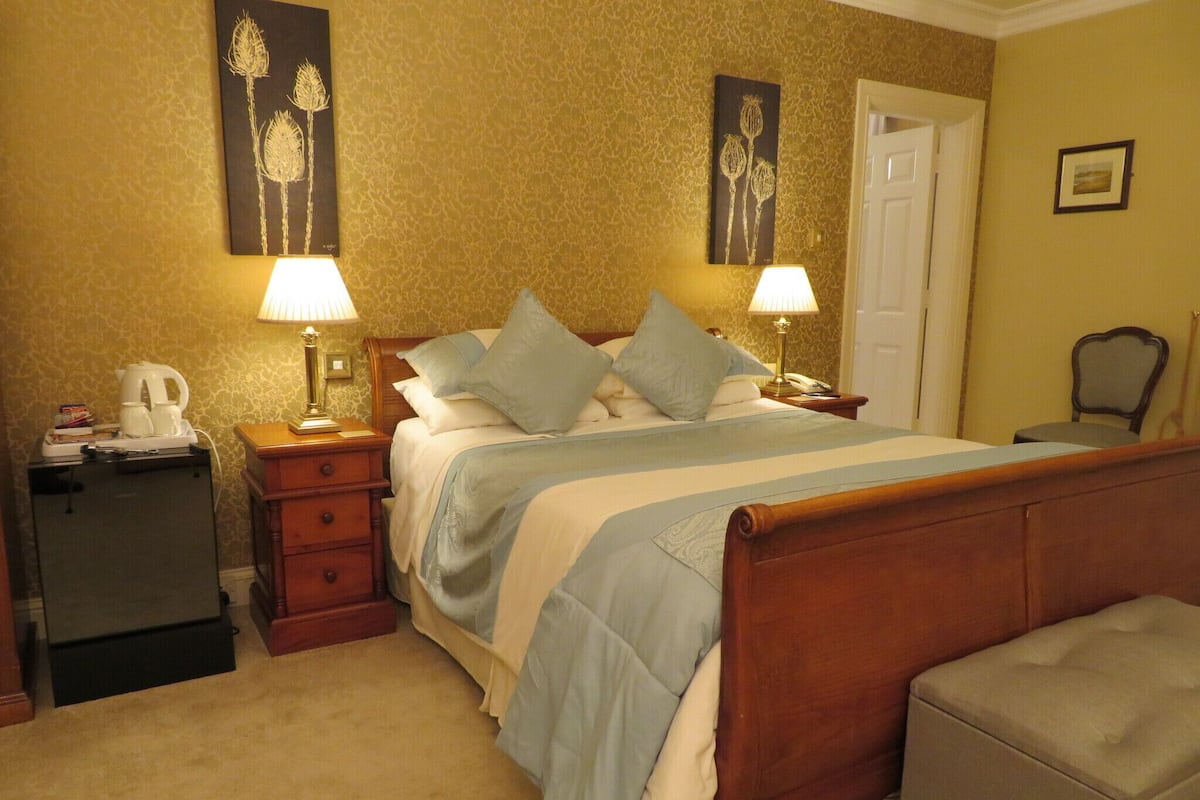 A neatly arranged hotel room with a bed, bedside tables, a lamp, a chair, and a small refrigerator.