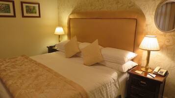 A hotel room with a large bed, two bedside lamps, a nightstand with a phone, and a mirror on the wall.