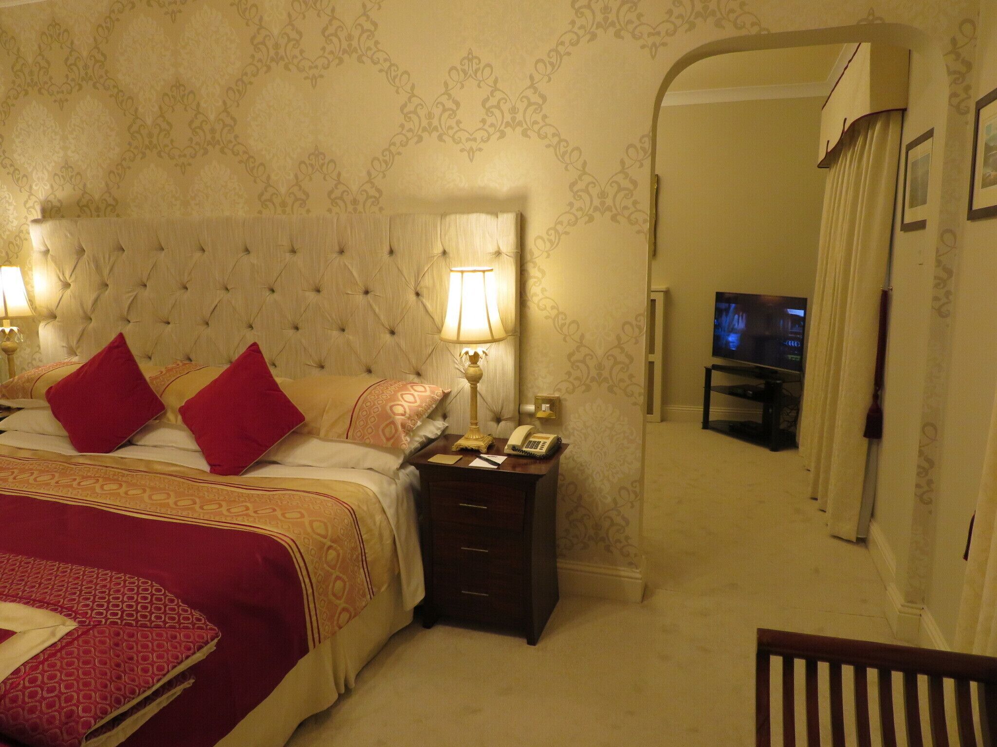 A hotel room with a large bed, two bedside lamps, a telephone, and a television in the corner.