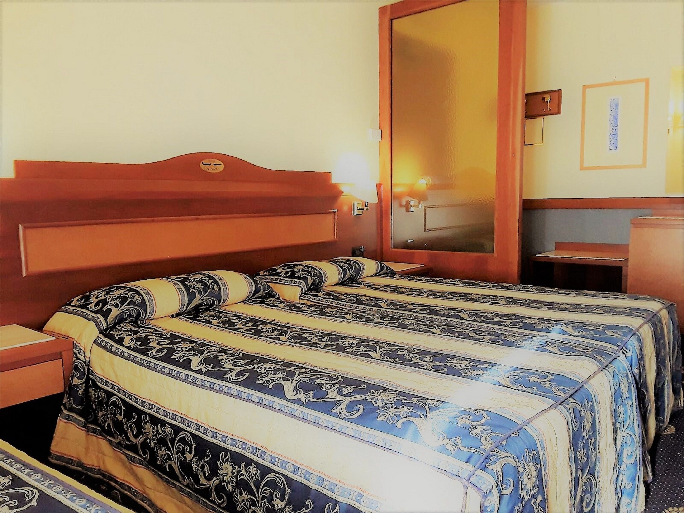 Ein Hotelzimmer mit einem großen Bett, einem Holzkopfende, einem Nachttisch, einem Schminktisch und einer kleinen Holzkommode.
