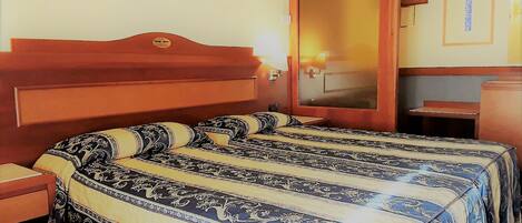 Una habitación de hotel con una cama grande, un cabecero de madera, una mesita de noche y un pequeño aparador de madera.