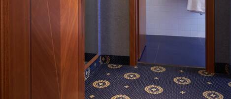 A hotel bathroom with a wooden door, a sink with a mirror, and a patterned floor.