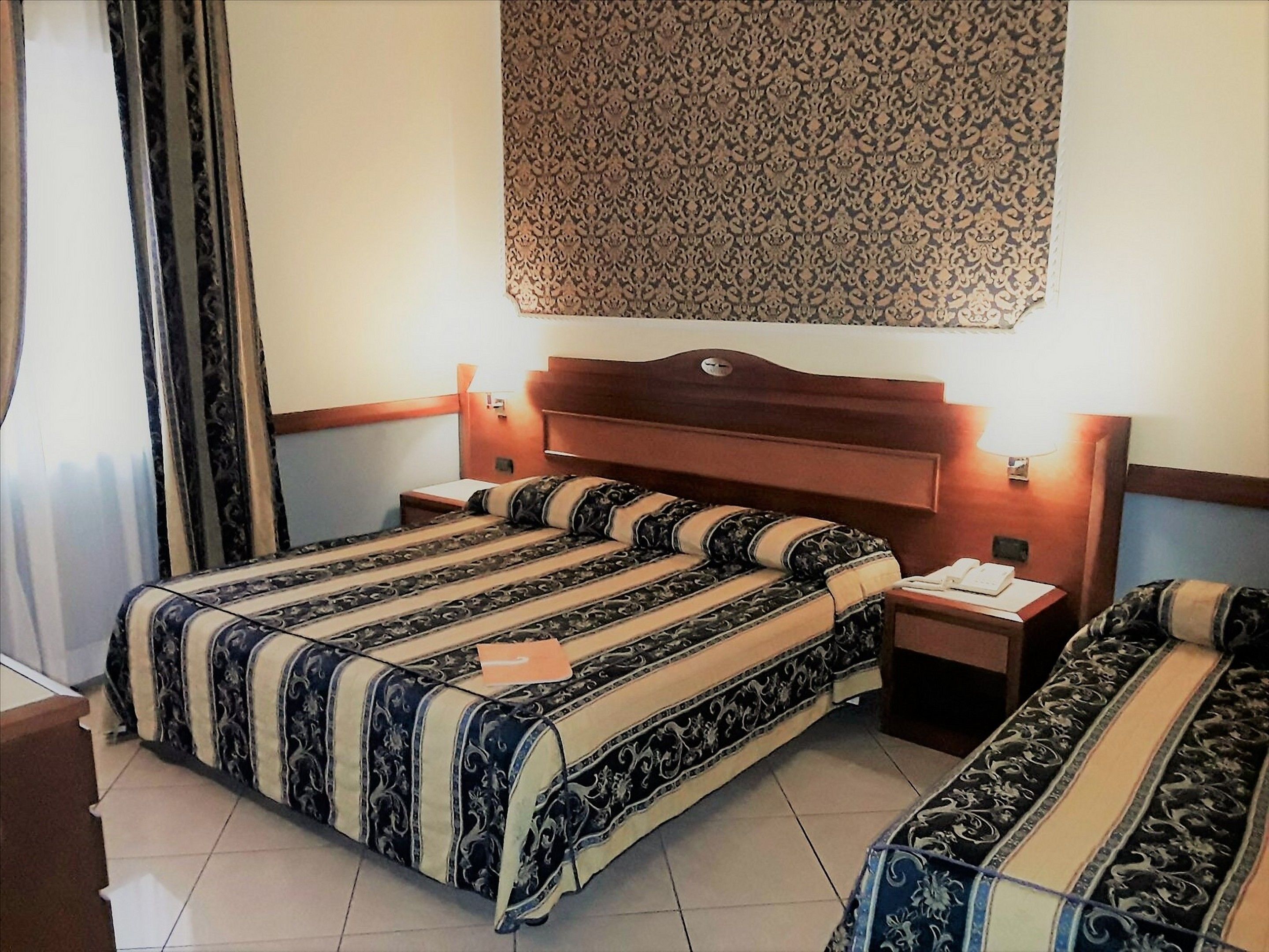 Una habitación de hotel con cama doble, mesita de noche y cabecera estampada.