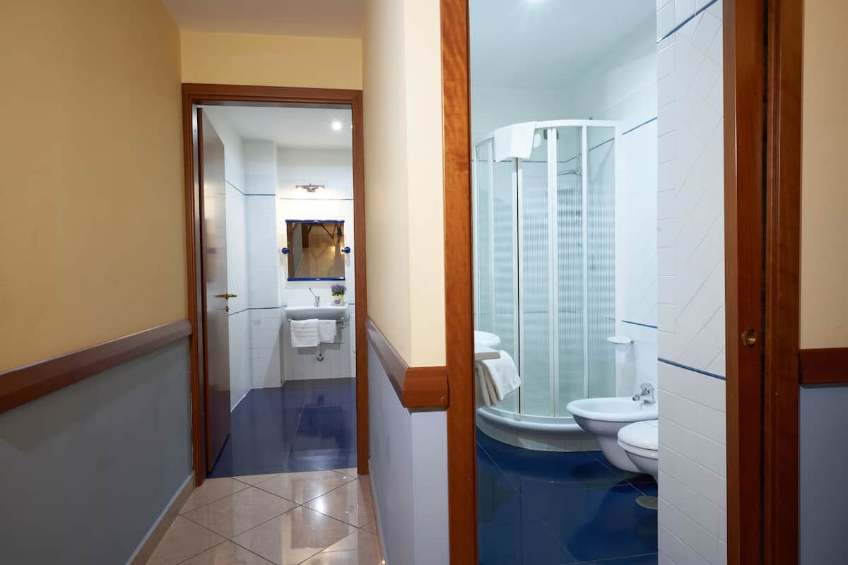 Un couloir étroit mène à une salle de bain équipée d’une douche, d’un lavabo et de toilettes.