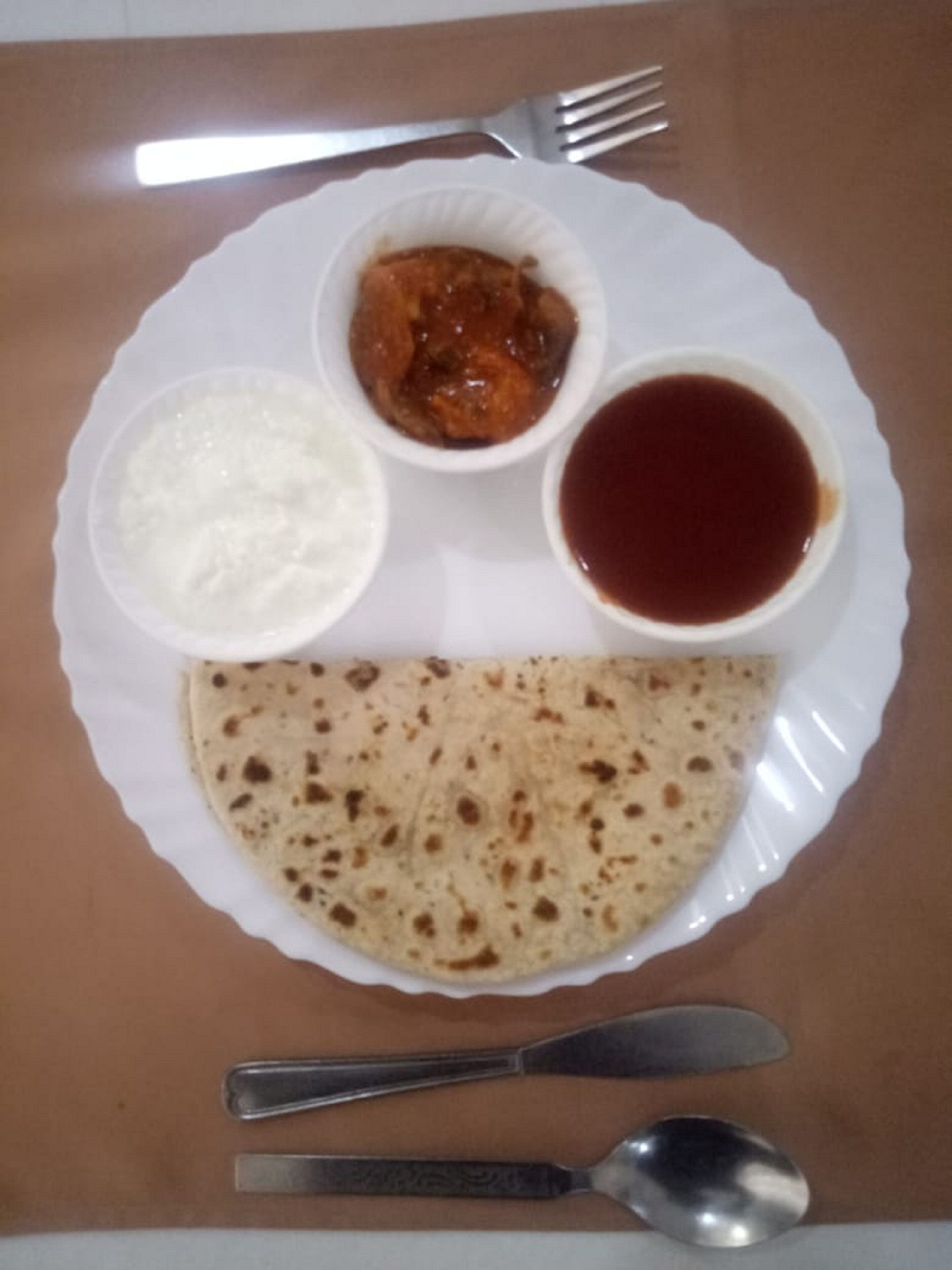 Un plato con pan plano, un tazón de arroz, un tazón de curry y un tazón de salsa.