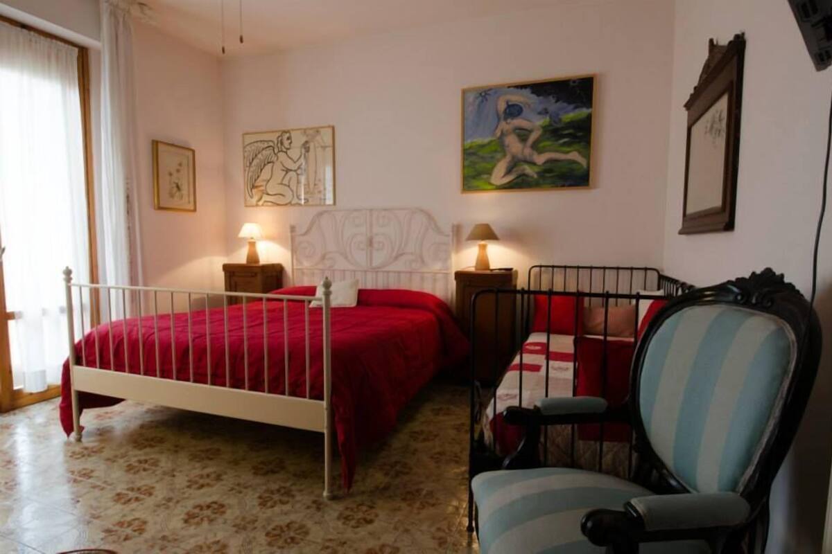 Une chambre avec un lit simple, une chaise et deux tables de chevet avec des lampes. On y trouve également des œuvres d’art murales et un tableau encadré au-dessus du lit.