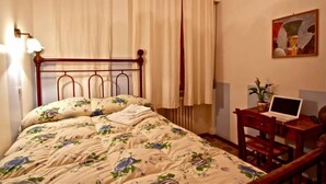 A bedroom with a floral bedspread, a wooden headboard, a desk with a laptop, and a painting on the wall. - Bed and Breakfast La Casa Di Elide (Arezzo)