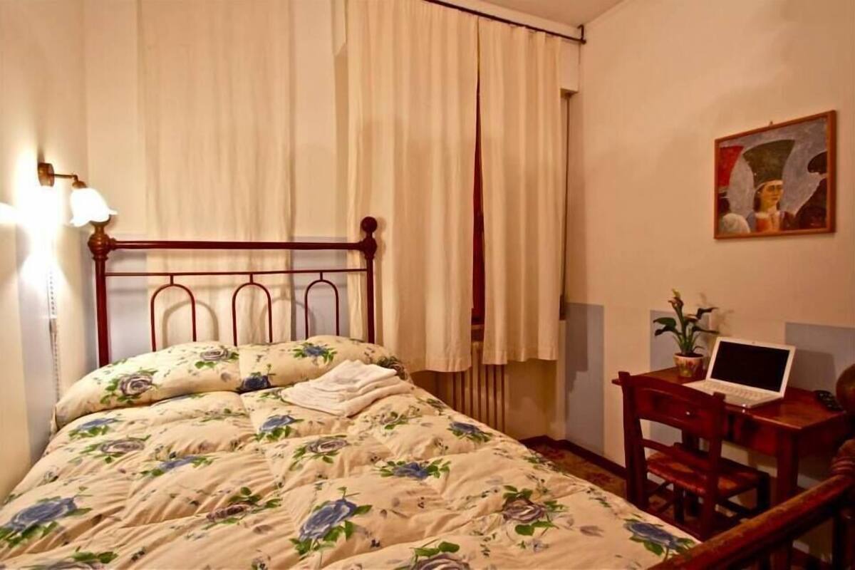 Une chambre à coucher avec une couvre-lit à motifs floraux, une tête de lit en bois, un bureau avec un ordinateur portable et un tableau accroché au mur.