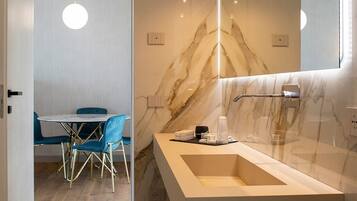 Un bagno moderno con zoccolo in marmo, uno specchio grande e un mobile lavabo. Si vede in secondo piano una zona pranzo con un tavolo rotondo e sedie.