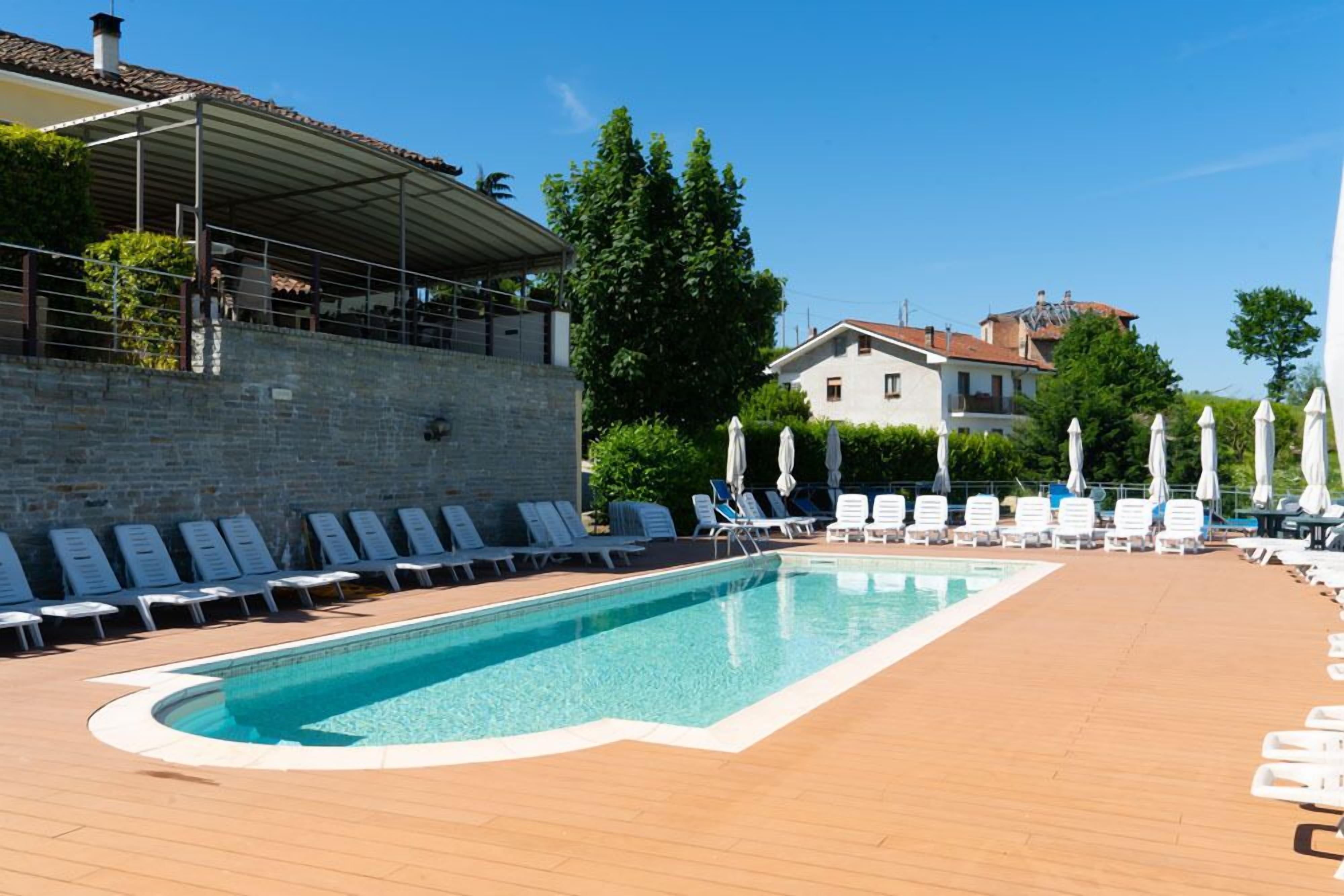 A swimming pool with lounge chairs and umbrellas, surrounded by a wooden deck and stone walls.