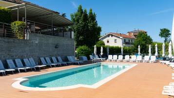 A swimming pool with lounge chairs and umbrellas, surrounded by a wooden deck and stone walls.