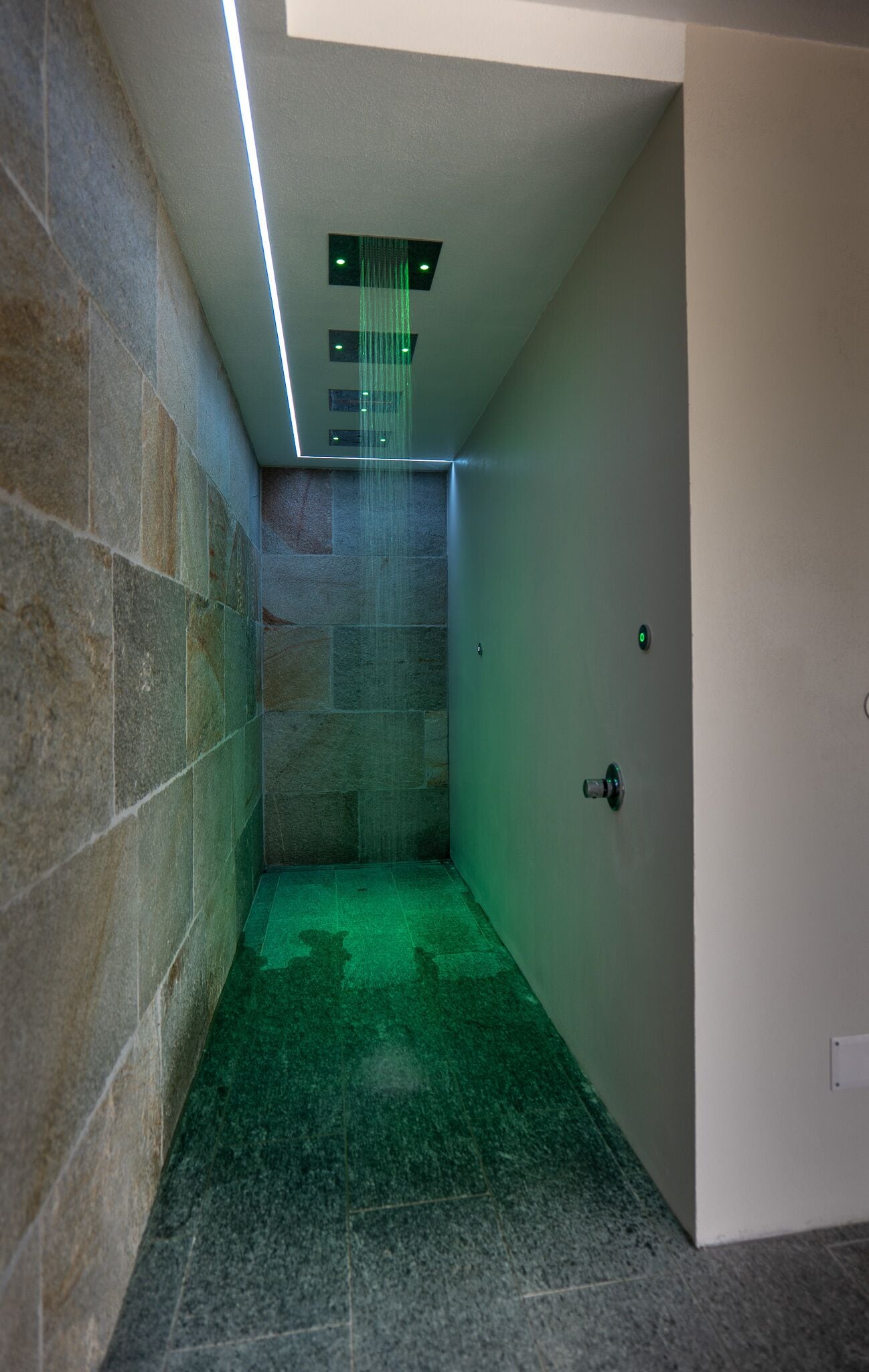 A modern bathroom with a shower area, stone walls, and a green light feature.
