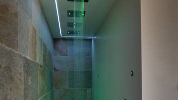 Une salle de bain moderne avec un espace douche, des murs en pierre et un éclairage d’ambiance vert.