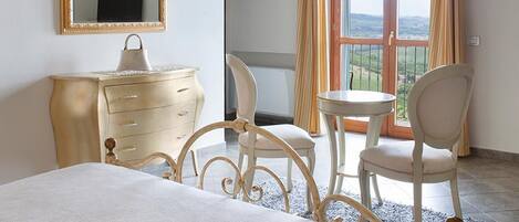A bedroom with a bed, a dresser, a chair, a table, a mirror, and a balcony with curtains.