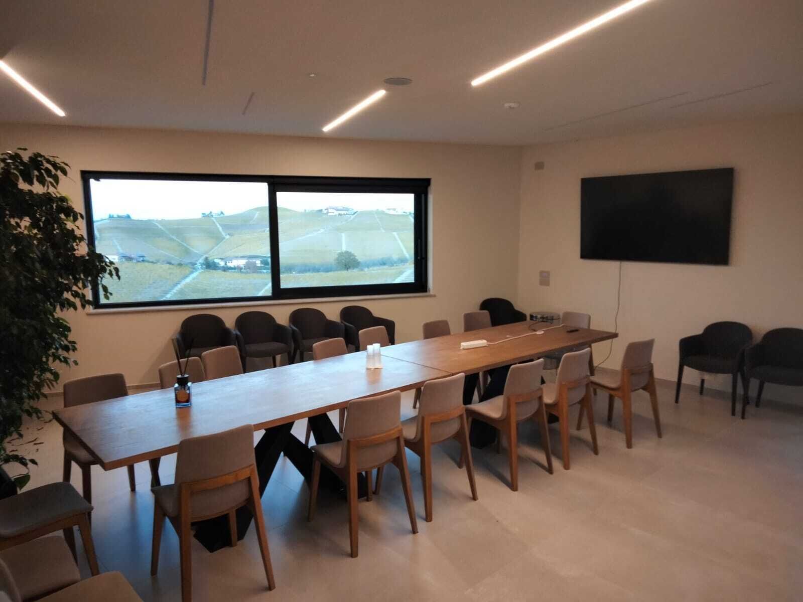 A conference room with a long table, multiple chairs, a large window with a view, and a flat-screen TV on the wall.