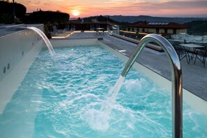 A swimming pool with water jets, surrounded by lounge chairs and tables, with a sunset view in the background. - Casa Nicolini Albergo Ristorante (Barbaresco)