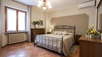 Une chambre à coucher avec un lit en métal, une commode en bois, un radiateur, une fenêtre avec des rideaux, un lustre et un climatiseur fixé au mur.