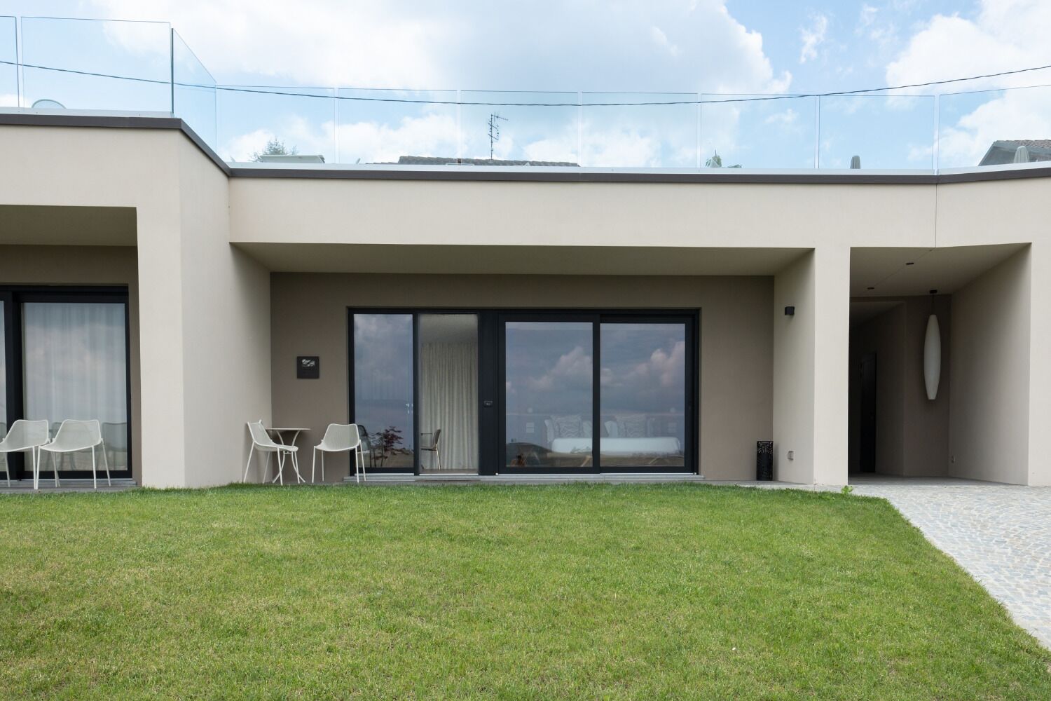 Un edificio moderno con tetto piatto, ampie porte scorrevoli in vetro e un piccolo patio con sedie e tavolo.