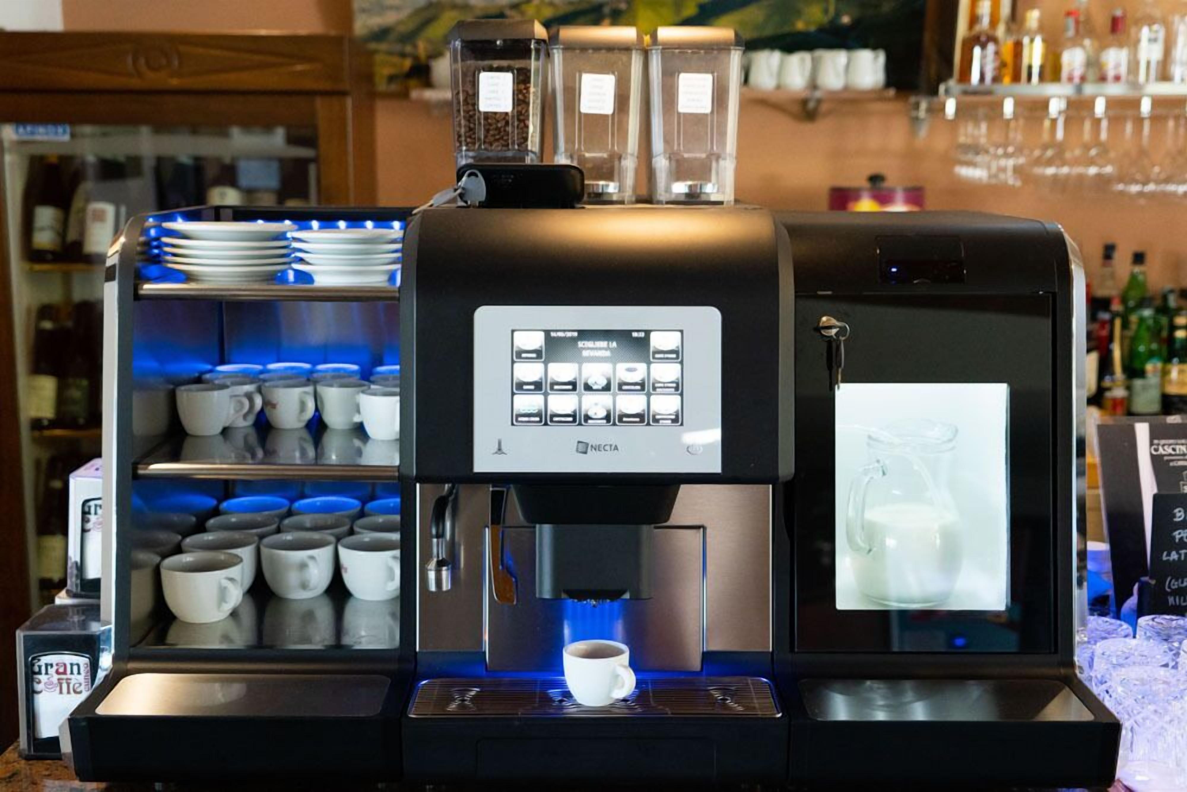 Una máquina de café con pantalla digital, una estación para espumar leche y una taza de café debajo.