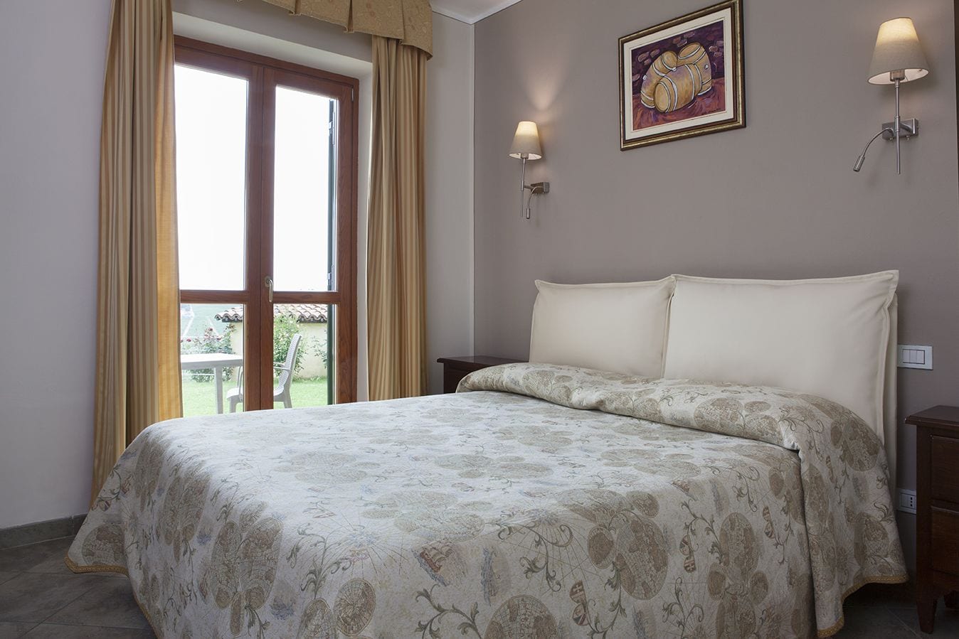 A bedroom with a large bed, a window with curtains, a wall-mounted lamp, and a framed picture.