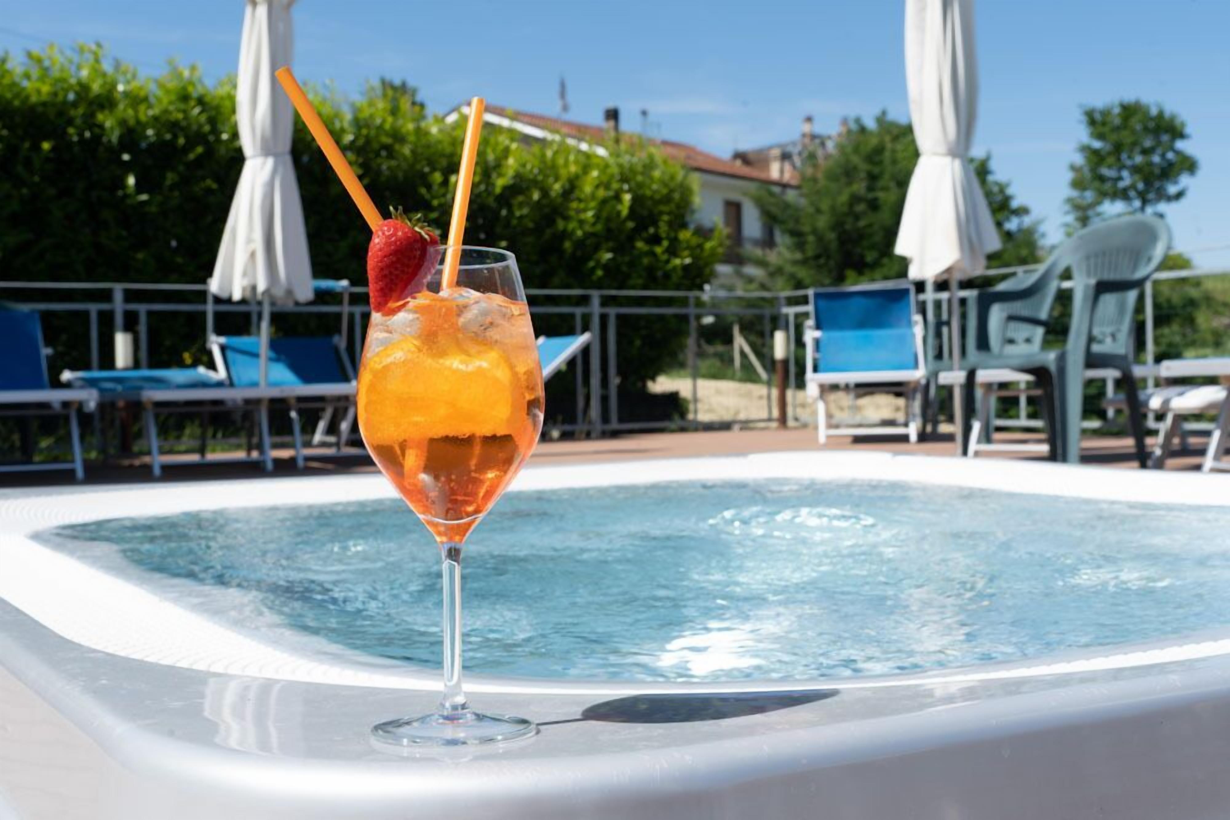 Un vaso de jugo de naranja con una fresa y una pajita sobre una mesa junto a la piscina.